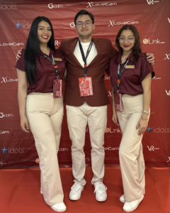 Three people are posing in front of a red backdrop at an event